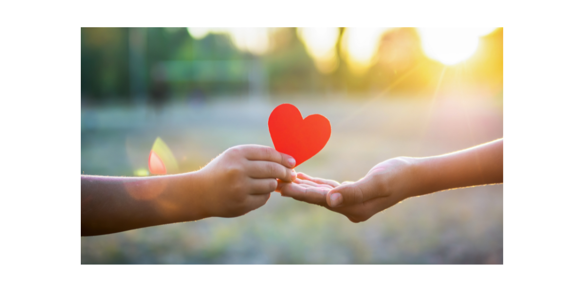 paper heart being passed from one person to another in front of a blurred field and setting sun
